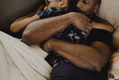High angle view of father embracing daughter while sleeping on sofa at home