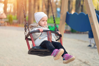 Cheerful cute girl sitting on swing at playground