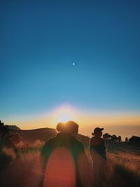 People on field against clear sky during sunset