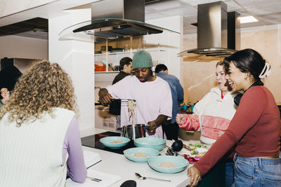 Multiracial young man and women with male friend serving noodles in college dorm