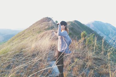 Side view of woman standing on mountain against sky