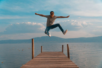 Man jumping on pier over sea against sky