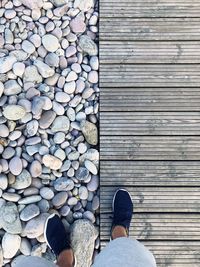 Low section of person standing on pebbles and boardwalk