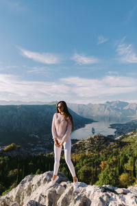 Full length of young woman standing on rock against sky