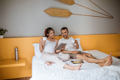 Portrait of smiling couple sitting on bed at home