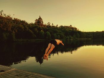 Reflection of woman jumping on lake against clear sky