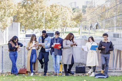 Students studying and using smart phones by railing on campus