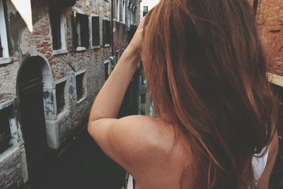 Rear view of woman with hand in hair standing against building