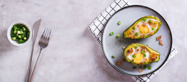 Egg baked in avocado sprinkled with bacon and herbs on a plate top view web banner