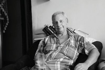 Portrait of happy senior man holding empty glass while sitting on chair