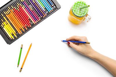 Close-up of hand holding pencils against white background