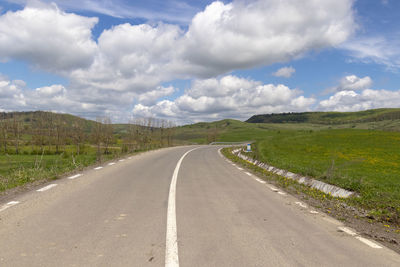 Empty road amidst field against sky