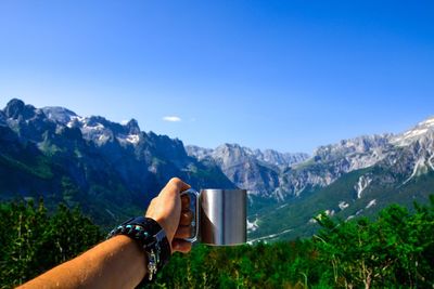 Cropped hand holding cup against mountains