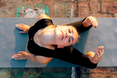 Young slender female in sports clothes doing raja bhujangasana while practicing yoga in city on sunny day