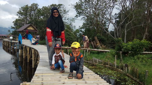 Portrait of mother with sons on footbridge by lake