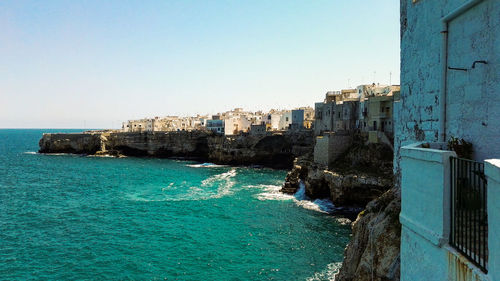 Buildings by sea against clear blue sky