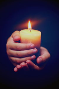 Cropped image of hands holding candle against black background