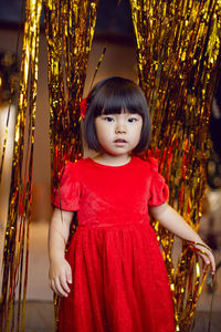 Portrait of a beautiful korean baby girl in a red dress at christmas with a gold decoration