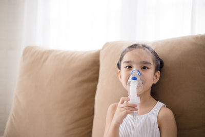 Portrait of boy drinking water on sofa at home