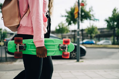 Midsection of young woman holding green skateboard while walking in city
