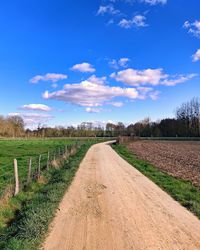 Road passing through agricultural field against sky