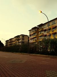 Street by buildings in city against sky during sunset