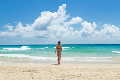 Rear view of woman standing at beach against sky