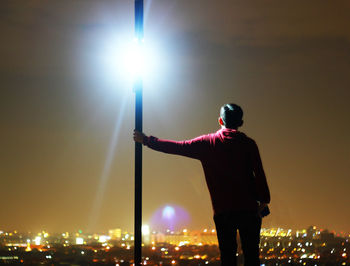 Rear view of silhouette man standing against illuminated sky at night