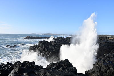 Panoramic view of sea waves splashing on rocks against sky