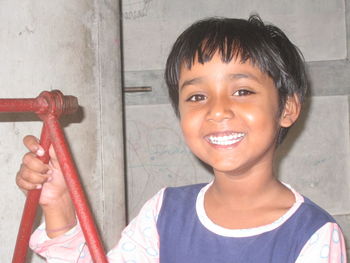 Close-up portrait of smiling girl standing against wall