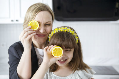Portrait of smiling mother and daughter holding orange slice against eye