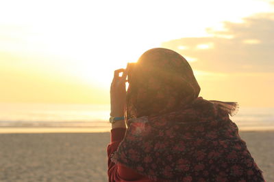 Rear view of woman on beach against sky during sunset