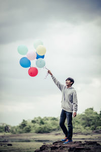 Full length of man holding balloons against sky