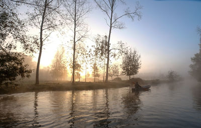 Man in boat on lake against sky during sunrise