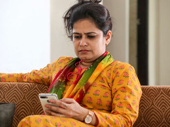 Mid adult woman using mobile phone while sitting on sofa