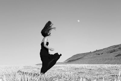 Side view of young woman with tousled hair standing on field against clear sky during sunny day