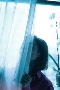 Portrait of young woman looking through window