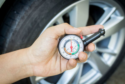 Cropped hand holding pressure gauge by car wheel 