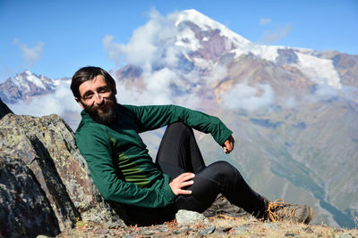 Young man sitting on rock against mountain