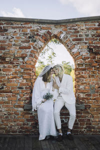 Smiling groom and bride sitting face to face on window sill in wedding