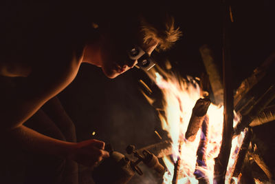 Man in protective eyewear holding equipment by bonfire at night