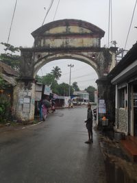 Rear view of man walking on road amidst buildings in city