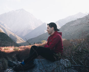 Side view of young man sitting on mountain