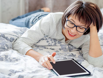 Woman in glasses are lying in bed with tablet. she is touching screen. morning at home.