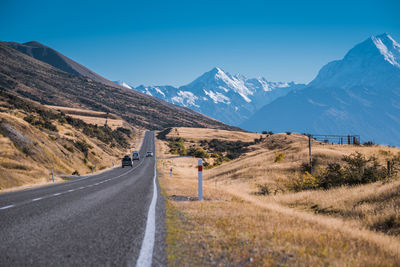 Road leading towards mountains against clear sky during sunny day