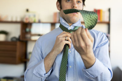 Confident man tying necktie at home