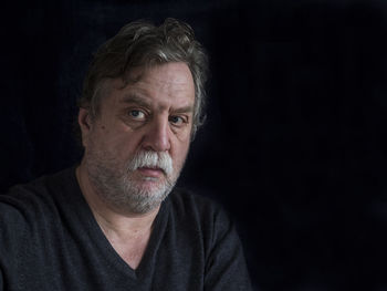 Portrait of serious mature man looking away against black background