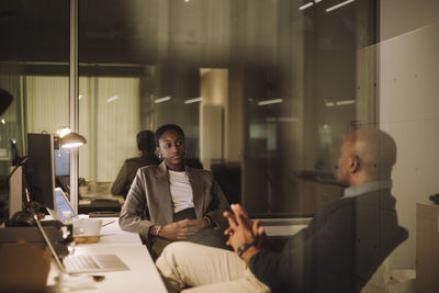 Mature businessman planning strategy with female colleague seen through glass of office