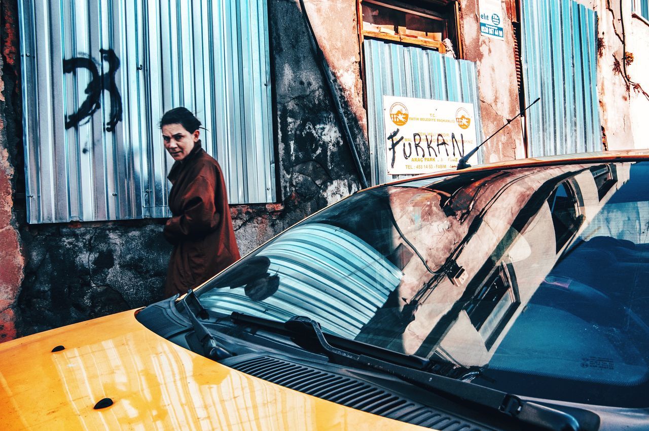 PORTRAIT OF YOUNG WOMAN STANDING ON CAR