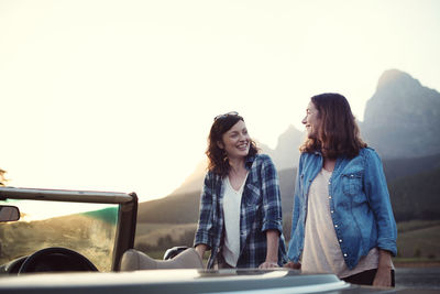 Female friends talking while standing by convertible car against clear sky